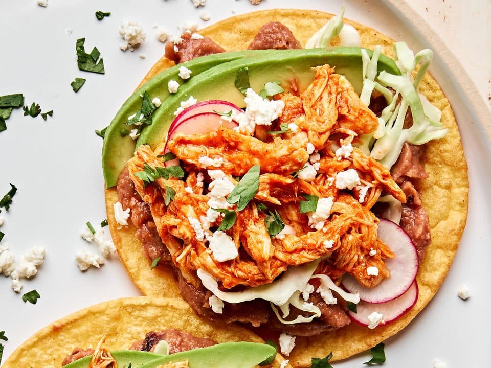 Chicken tinga tostadas topped with avocado, tomato and crema